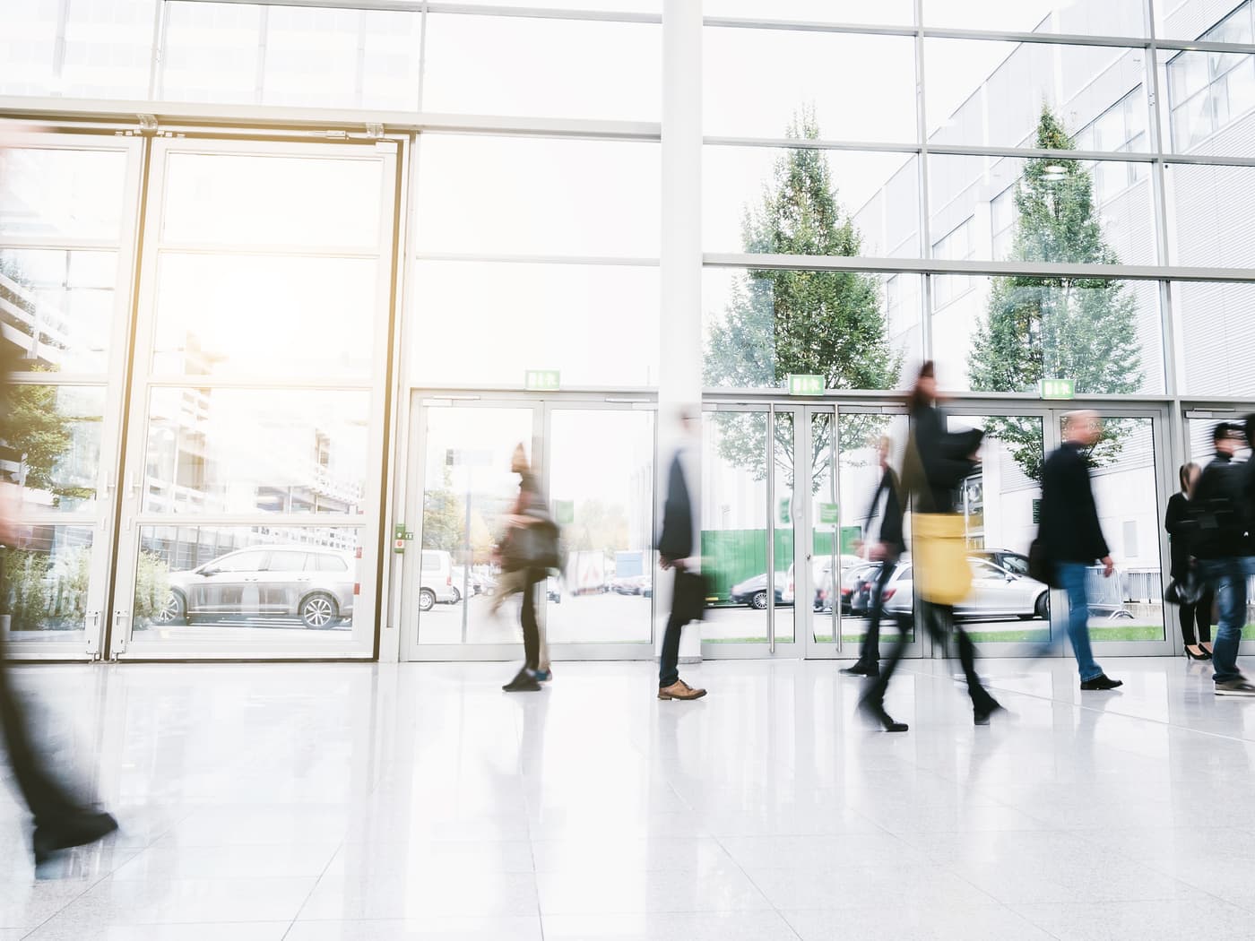 People crossing a glass-fronted lobby, most caught in motion blur