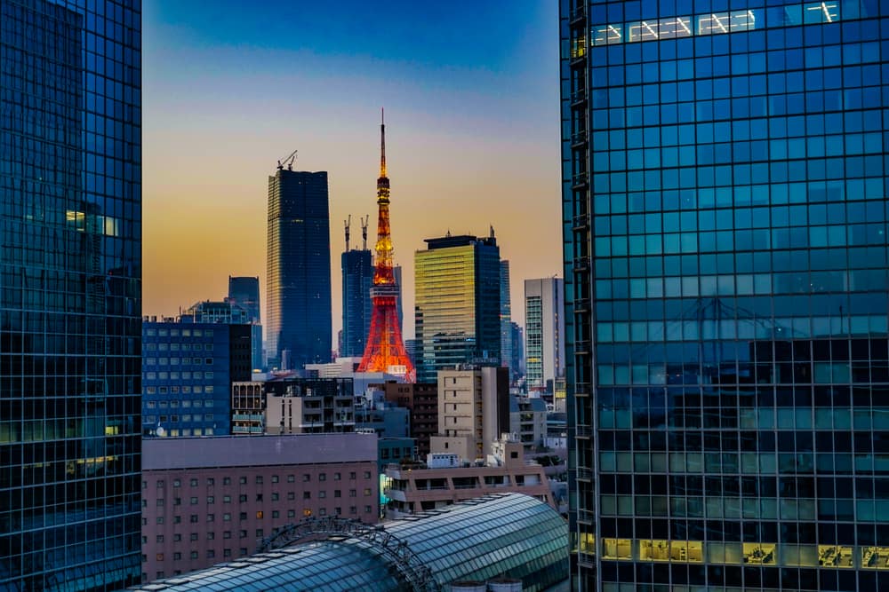 Tokyo Tower lit orange at dusk between two glass office towers in central Tokyo